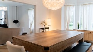 Ein moderner Essbereich mit Holztisch, Stühlen, einer Bank, einem Klavier und einer großen, flauschigen Leuchte.