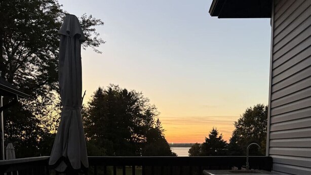 Eine Holzterrasse mit Waschbecken und kleinem Tisch, mit Blick auf ein Gewässer bei Sonnenuntergang.