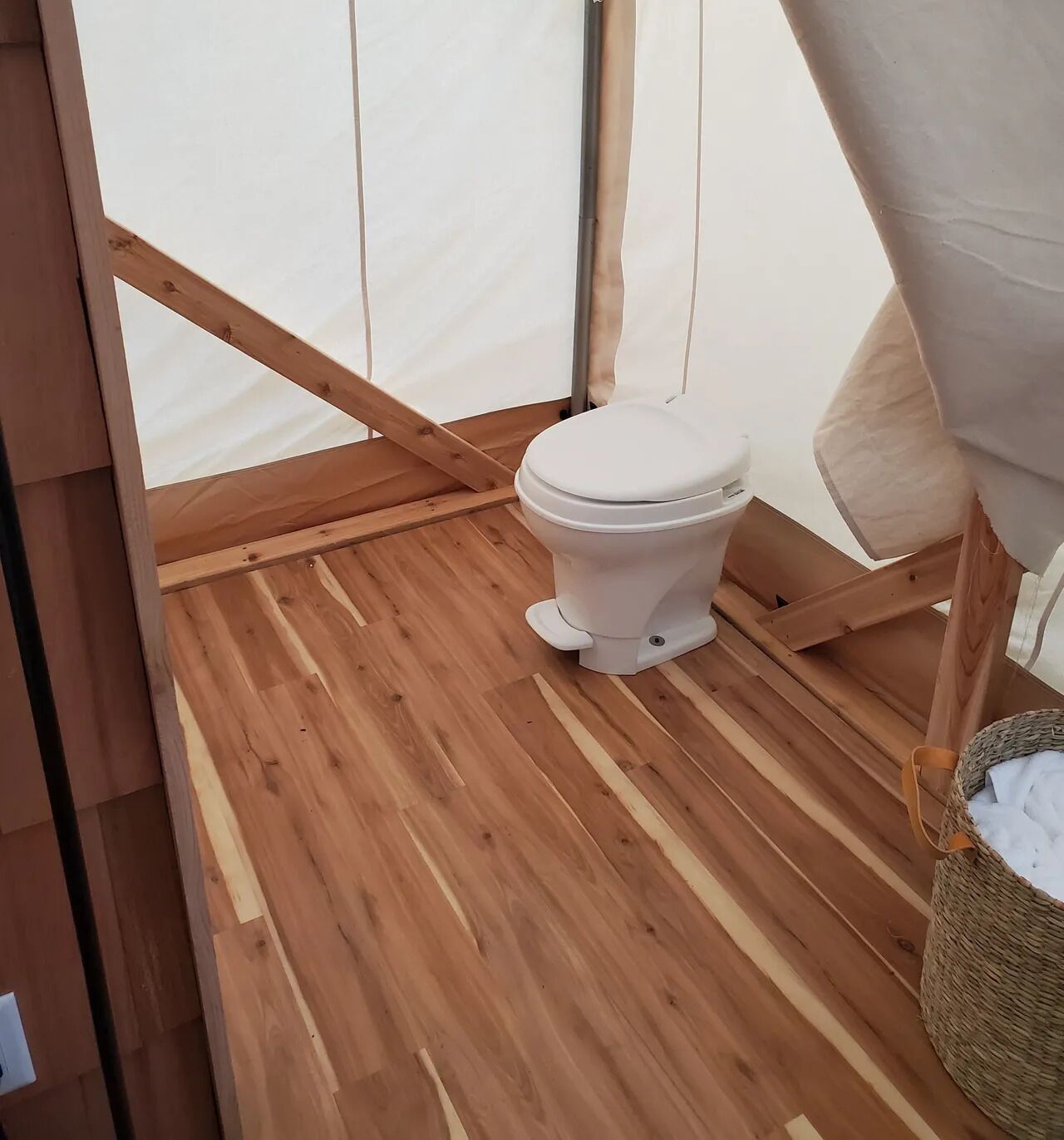 Un piso de madera, un inodoro blanco y una cesta tejida con objetos blancos.