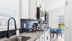 Una cocina moderna con un lavamanos de acero inoxidable, armarios blancos y un salpicadero de azulejos azules.
