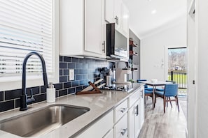 A modern kitchen with a stainless steel sink, white cabinets, and a blue-tiled backsplash. - North Fork Resort (Greenport)