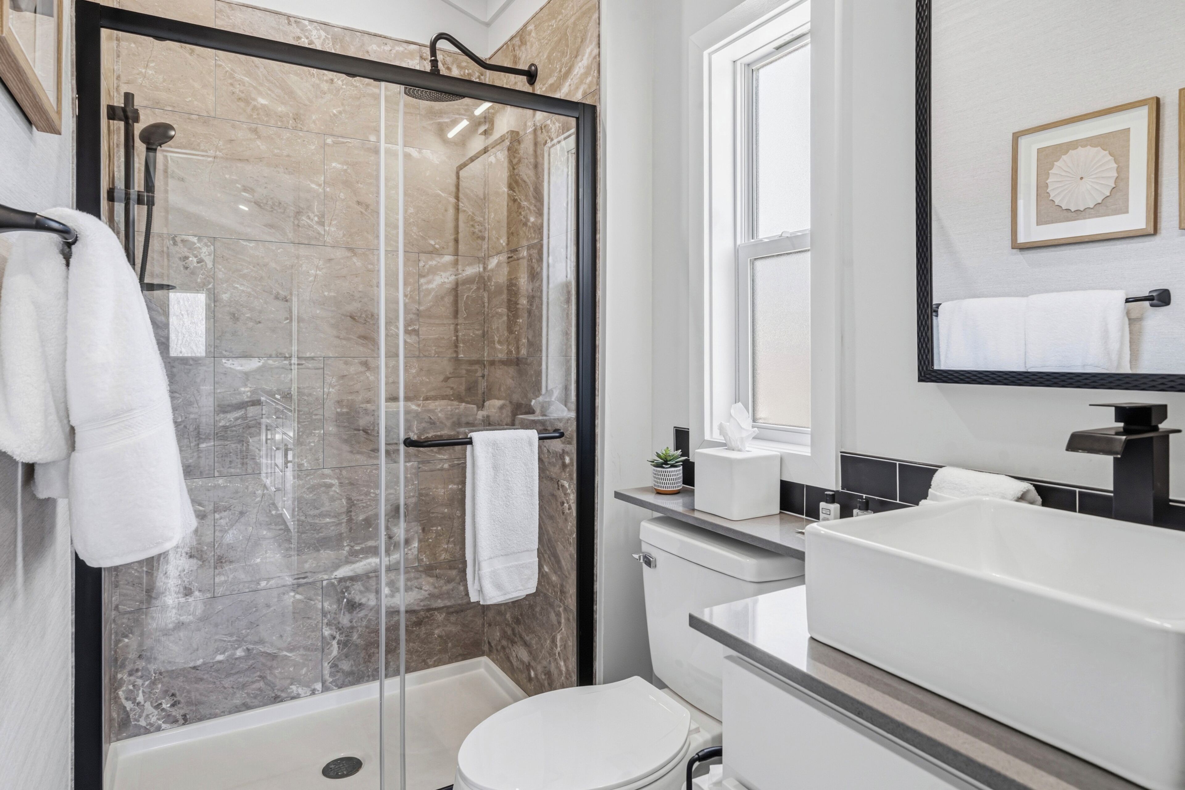Een moderne badkamer met een douchecabine van glas, een witte badkuip, toilet en een wastafel met spiegel erboven.