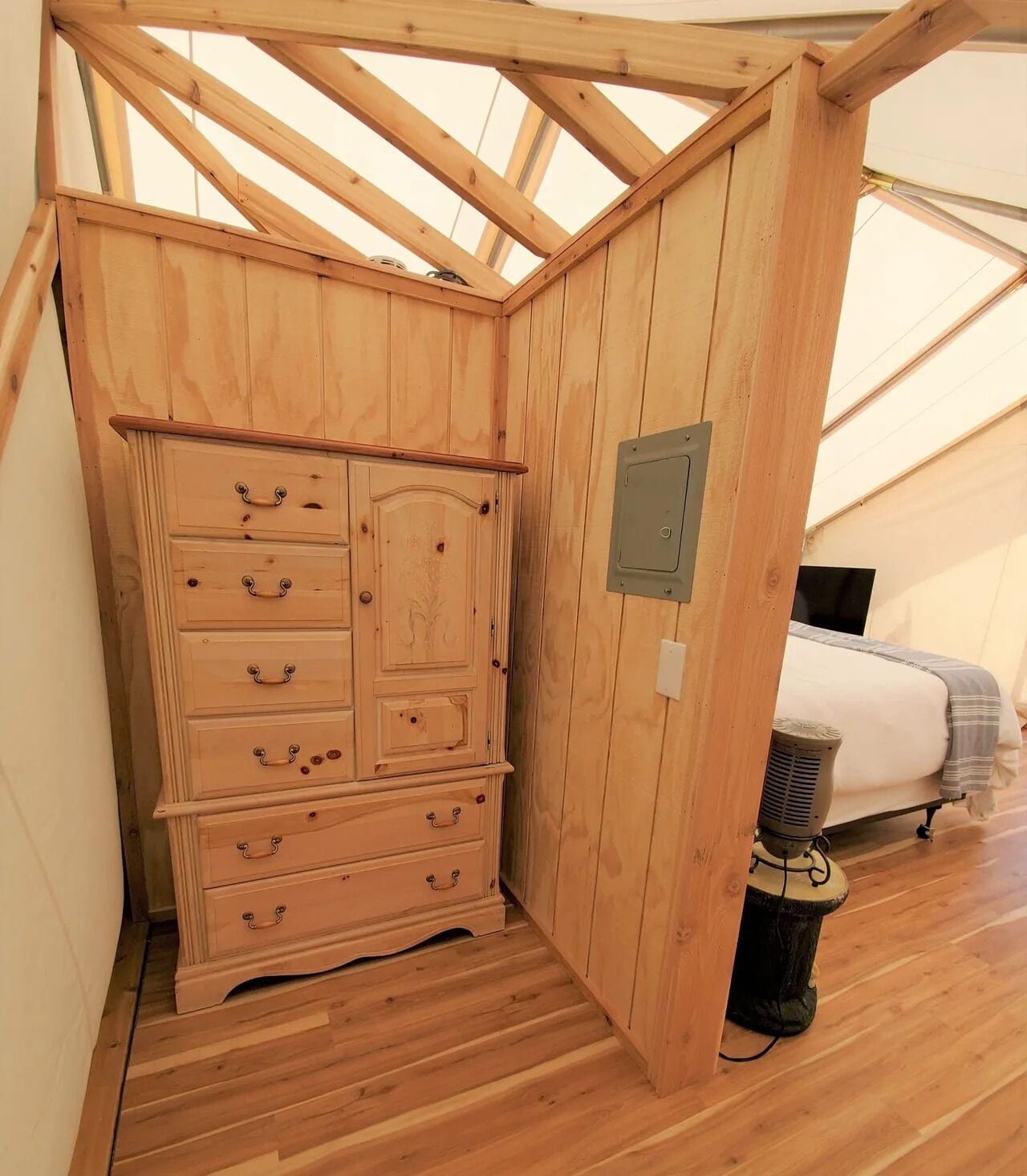 A wooden cabinet with drawers and a radiator in a tent-like room with a bed.