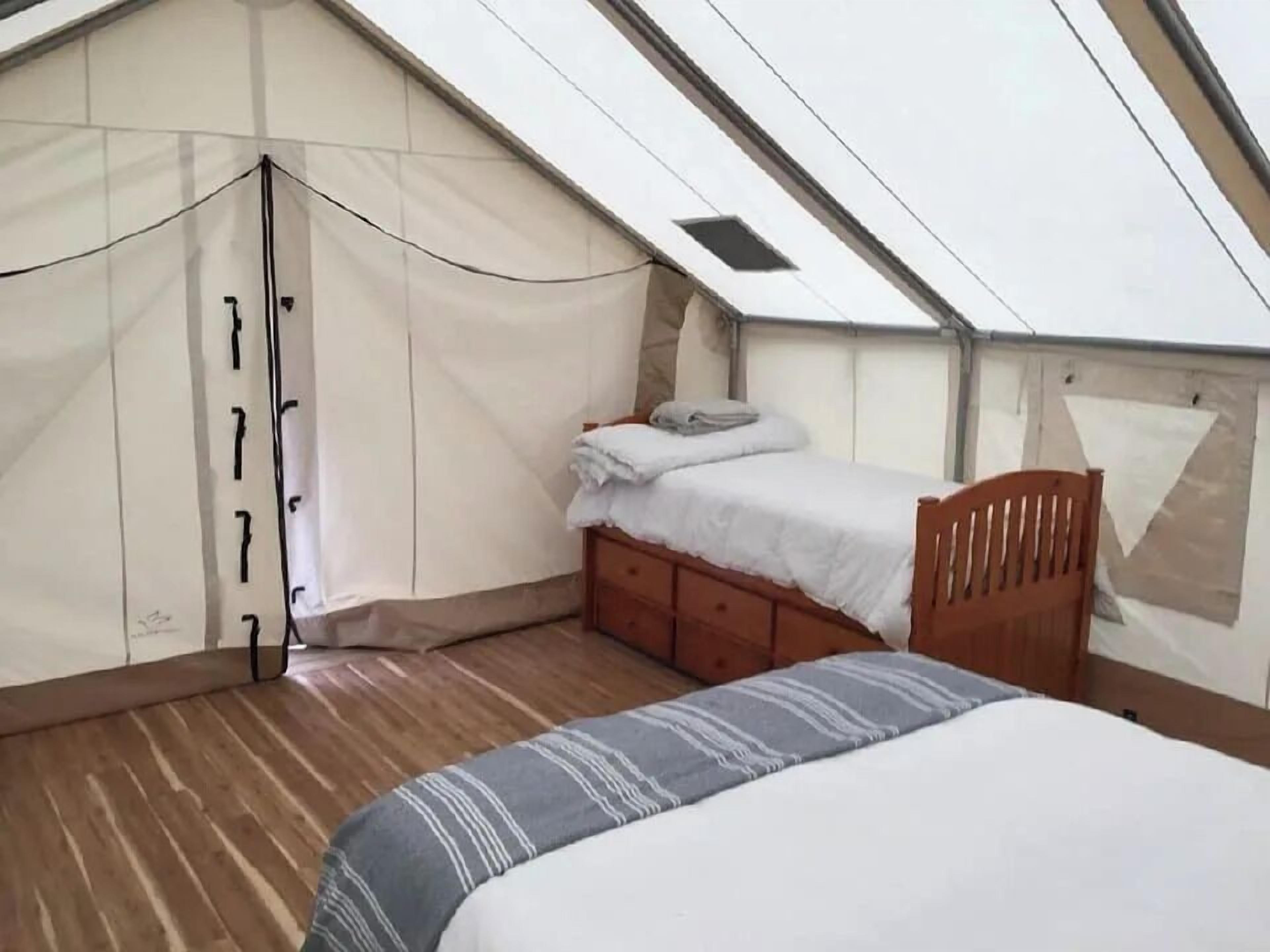 A tented room with a bed, a wooden wardrobe, and a bench.