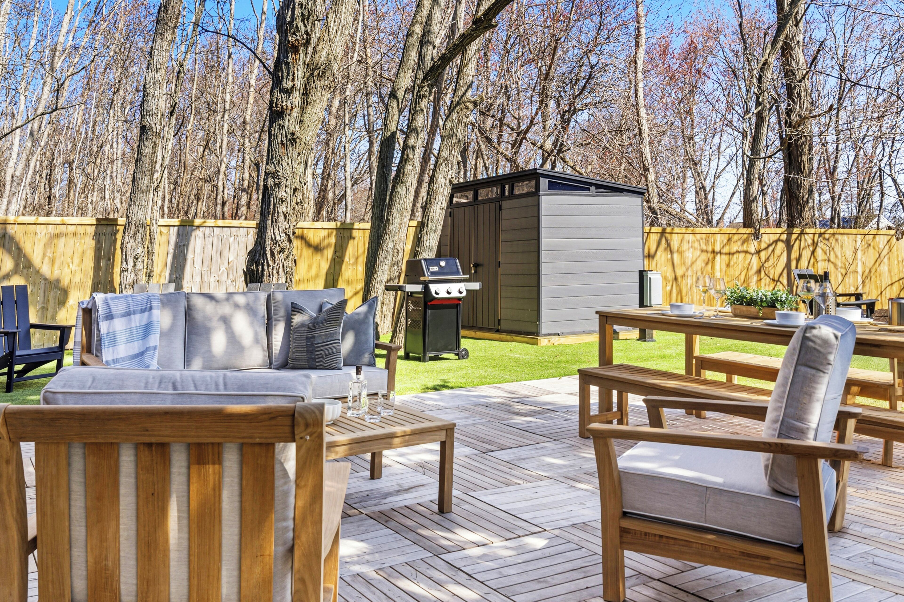 A deck with wooden furniture, a barbecue grill, and a shed.
