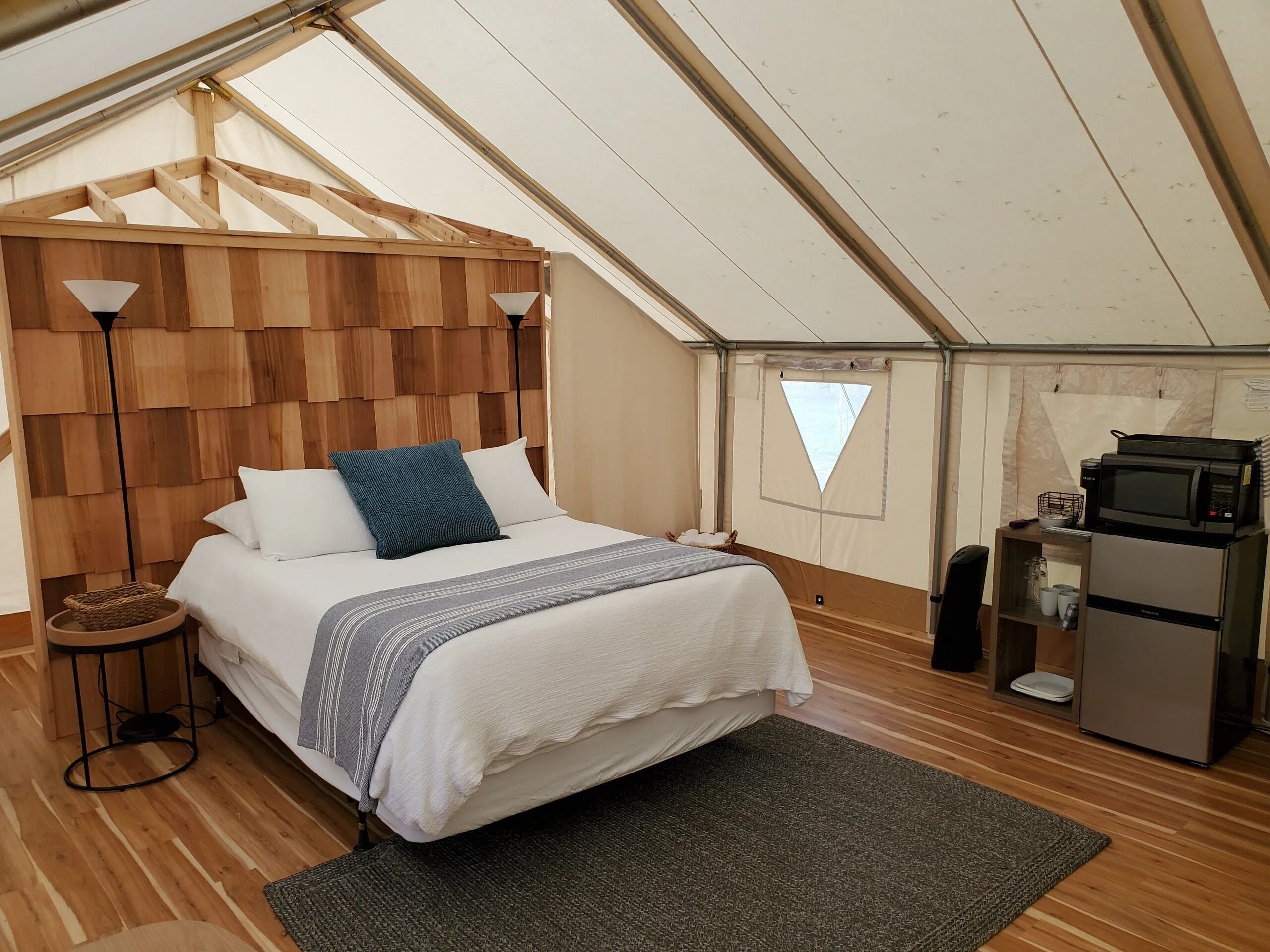 Un dormitorio acogedor con cama, lámparas de noche, una mesita y una kitchenette con microondas y refrigerador.
