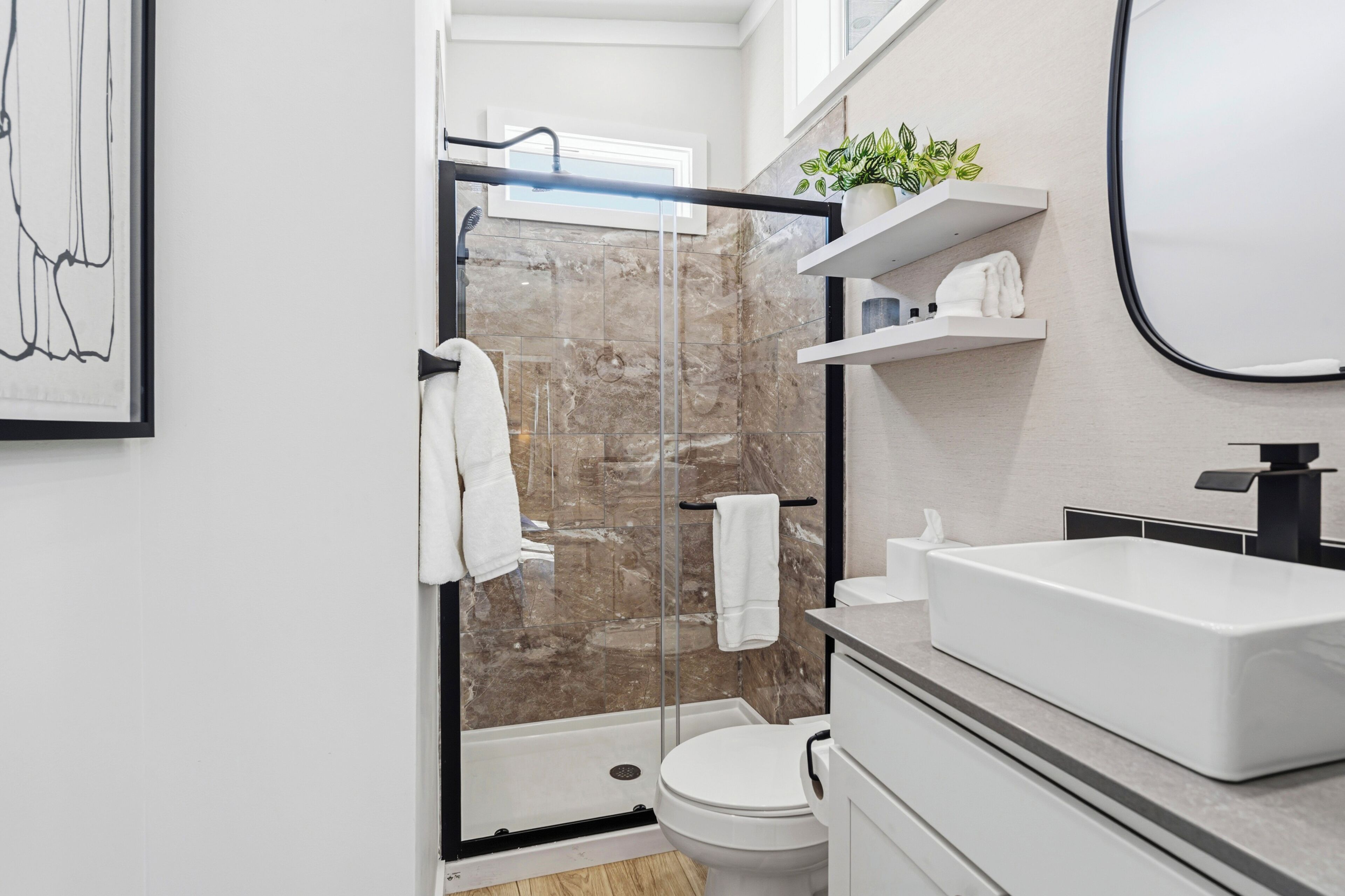 Une salle de bain moderne avec une douche à parois de verre, des toilettes blanches et un lavabo blanc doté d’un robinet noir.