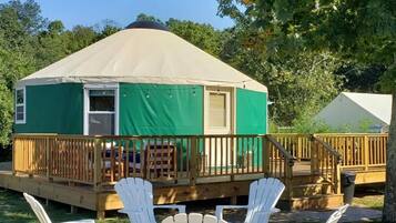 A green and beige yurt with a wooden deck and white Adirondack chairs.