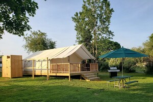 A tented accommodation with a wooden deck, a barbecue area, and a picnic table.