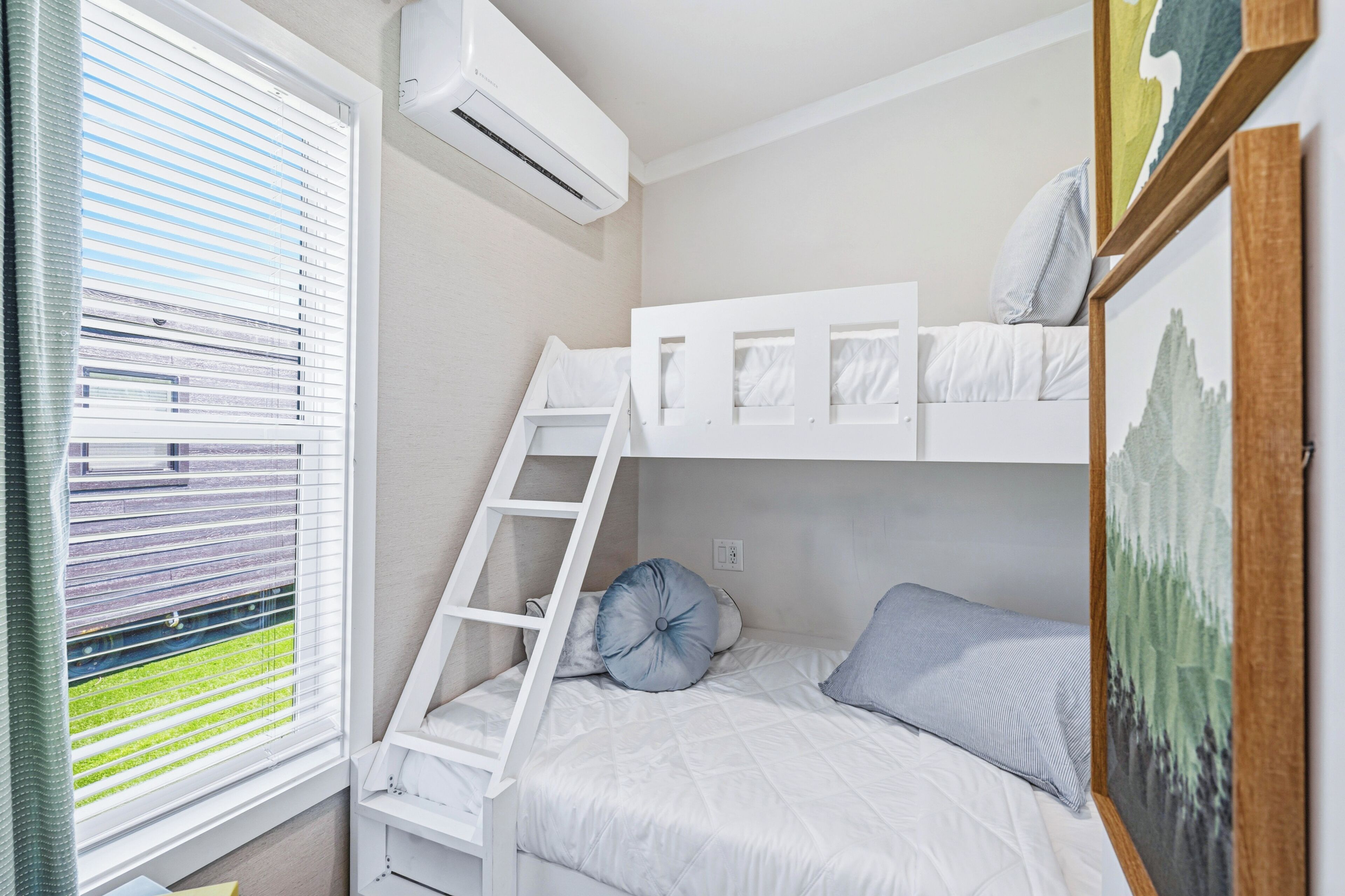 A bunk bed room with a ladder, white bedding, and a window with blinds.