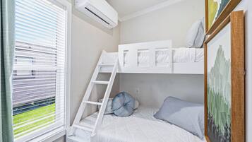 A bunk bed room with a ladder, white bedding, and a window with blinds.