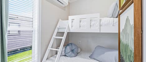 A bunk bed room with a ladder, white bedding, and a window with blinds.