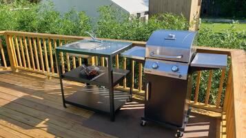 A wooden deck with a glass-top table and a portable grill.