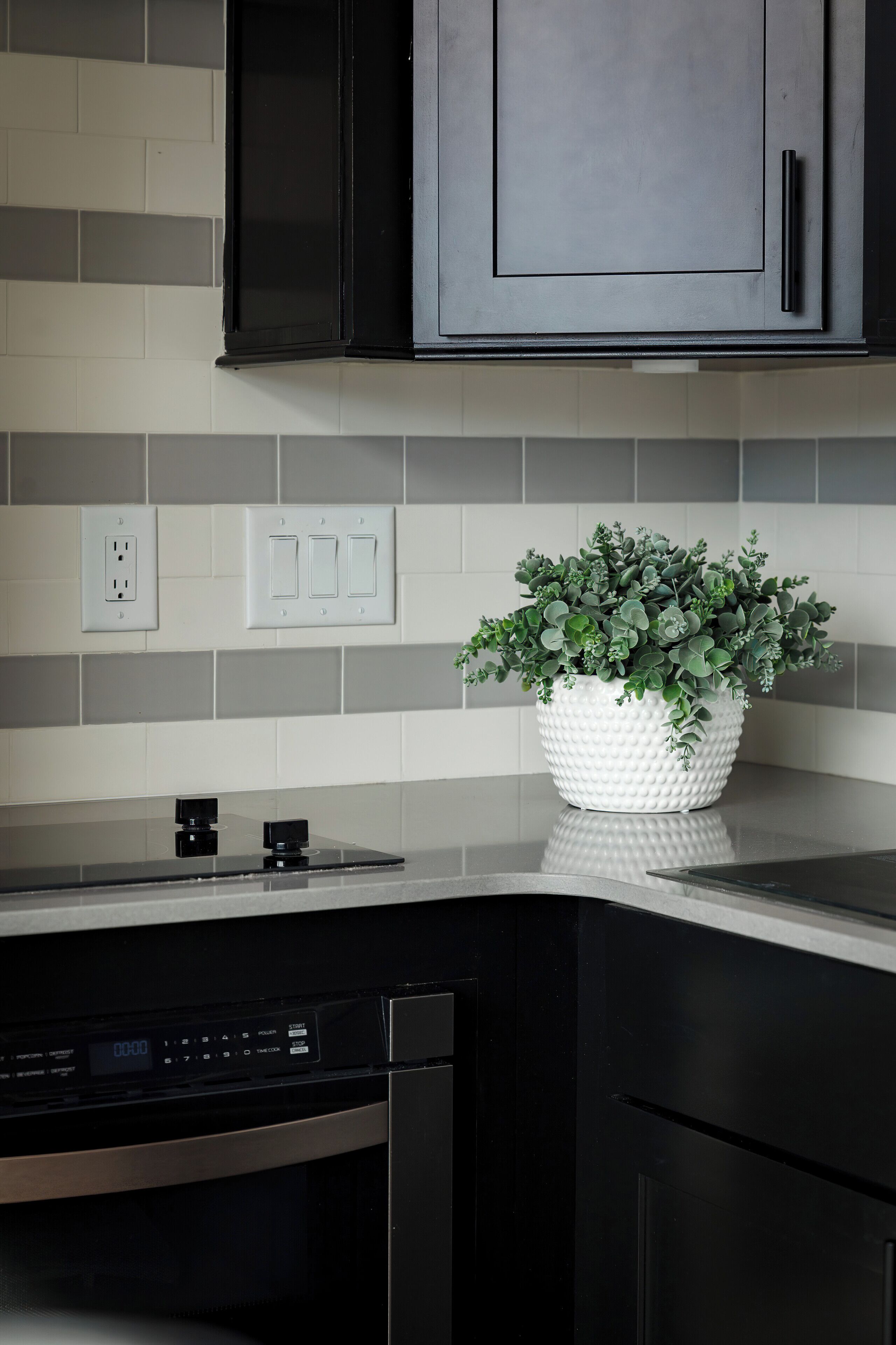 A modern kitchen with a black dishwasher, a white textured planter with green plants, and a tiled backsplash.