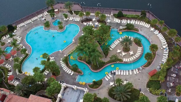 An aerial view of a resort with multiple interconnected swimming pools, sun loungers, and palm trees. - Christmas time at Disney (Orlando)
