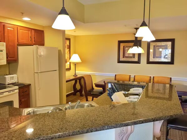 A kitchen with granite countertops, a refrigerator, a microwave, and a dining area with a table and chairs.