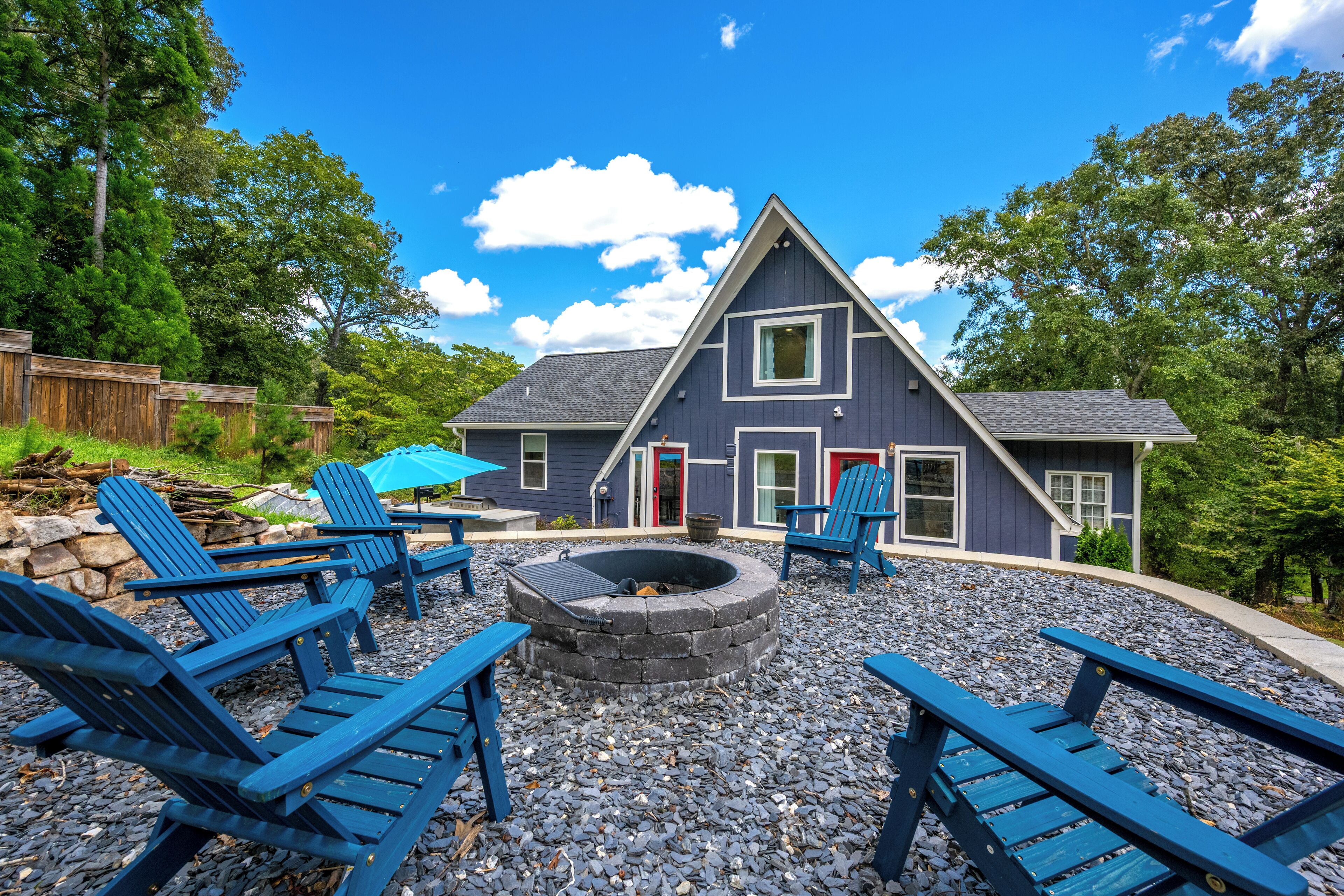 A house with a stone fire pit, blue Adirondack chairs, and a red door.