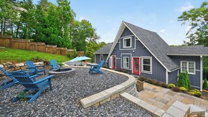 A house with a grey roof, red doors, and a stone fire pit surrounded by blue Adirondack chairs. - Lake house views, w/dock in quiet cove, new renovations & great outdoors spaces! (Dahlonega)