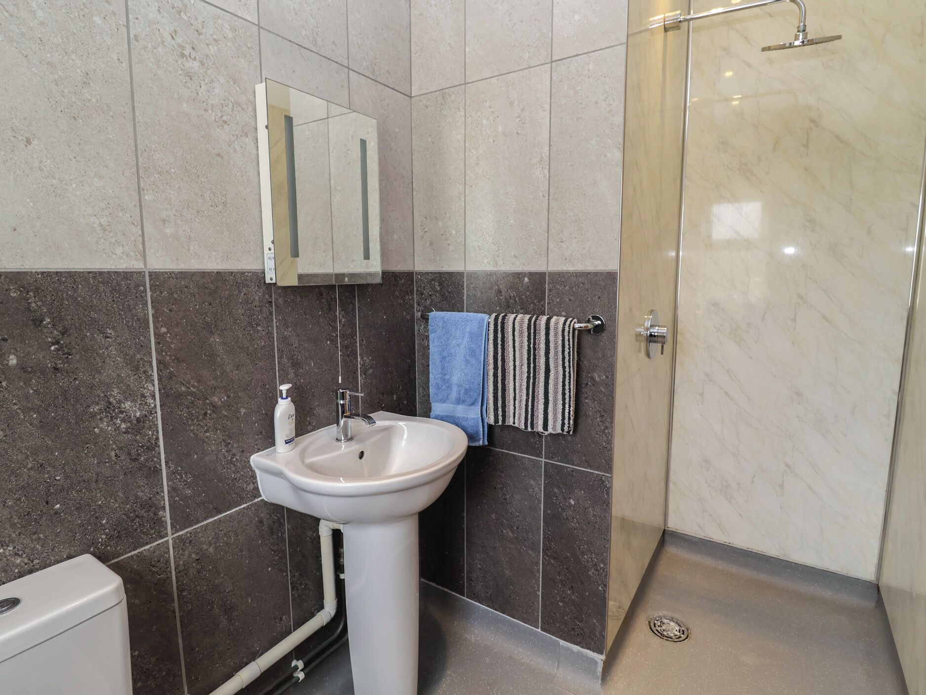 Een badkamer met wastafel, spiegel, handdoekhouder en douche.
