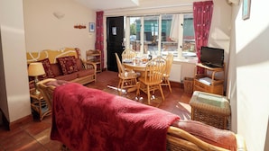 A cozy living room with a sofa, dining table, chairs, and a TV. - Coachman's Cottage (Ipswich)