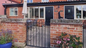 A two-story brick house with a black front door, a visible sign reading "Coachman's Cottage," and a gated entrance. - Coachman's Cottage (Ipswich)