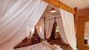 A four-poster bed with a floral bedspread, white curtains, and a wooden headboard. - Coachman's Cottage (Ipswich)