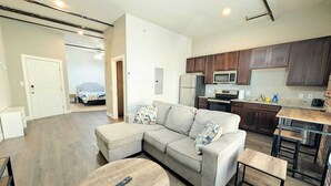 A modern living room with a sectional sofa, a round coffee table, and a kitchen area with wooden cabinets and stainless steel appliances.