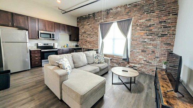 A modern living room with a sectional sofa, a round coffee table, and a brick wall.