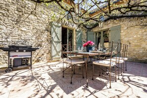 An outdoor dining area with a stone wall, a grill, and a table set for four with chairs. - Lantisse, luxury holiday home (Dégagnac)