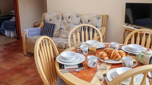 A dining area with a table set for breakfast, including croissants, coffee, and tea. There is a sofa with cushions and a television in the background. - Churn House (Ipswich)