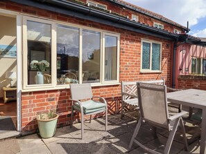 A patio with a table and chairs, a potted plant, and a window with a view of the street. - Churn House (Ipswich)