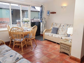 A cozy dining area with a wooden table and chairs, a wicker sofa, and a tiled floor.