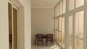 A corridor with a dining table and chairs, large windows, and a ceiling fan.