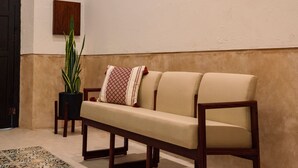 A beige sofa with a patterned pillow, a wooden bench, and a potted plant in a corner. - Renovated colonial house in Campeche's historic center (San Francisco de Campeche)