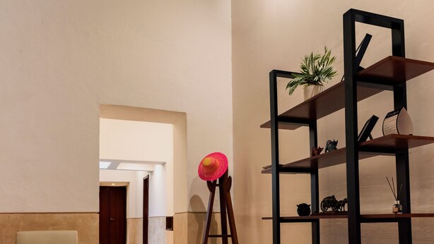 A hallway with a wooden chair, a standing lamp with a red hat, and a black shelving unit with decorative items. - Renovated colonial house in Campeche's historic center (San Francisco de Campeche)
