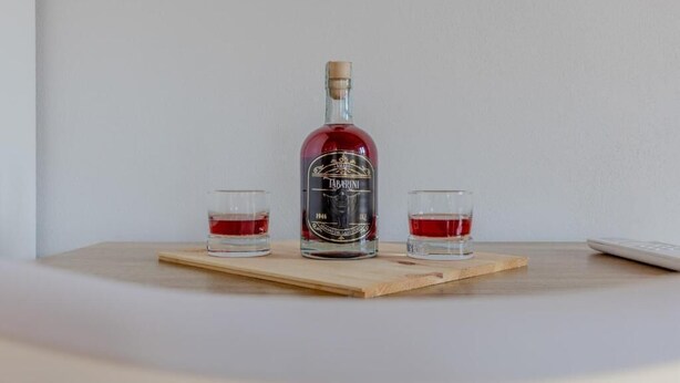 A bottle of Tabarnis liquor on a wooden board with two shot glasses filled with the drink. - Casa Tabarini (Pettenasco)