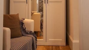 A room with a large white wardrobe, a striped chair, and a wooden floor.