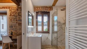 A modern bathroom with a glass shower, a sink, and a window overlooking a scenic view.