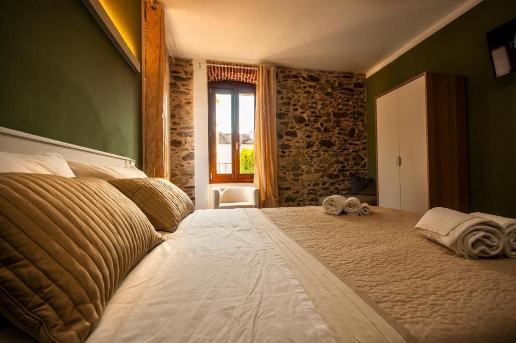Une chambre avec un grand lit, un mur en pierre et une fenêtre avec des rideaux.