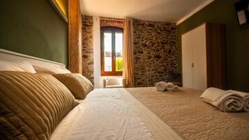 Une chambre avec un grand lit, un mur en pierre et une fenêtre avec des rideaux.