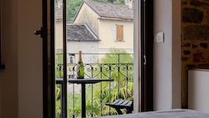 A balcony with a table and a bottle, overlooking a house and greenery.