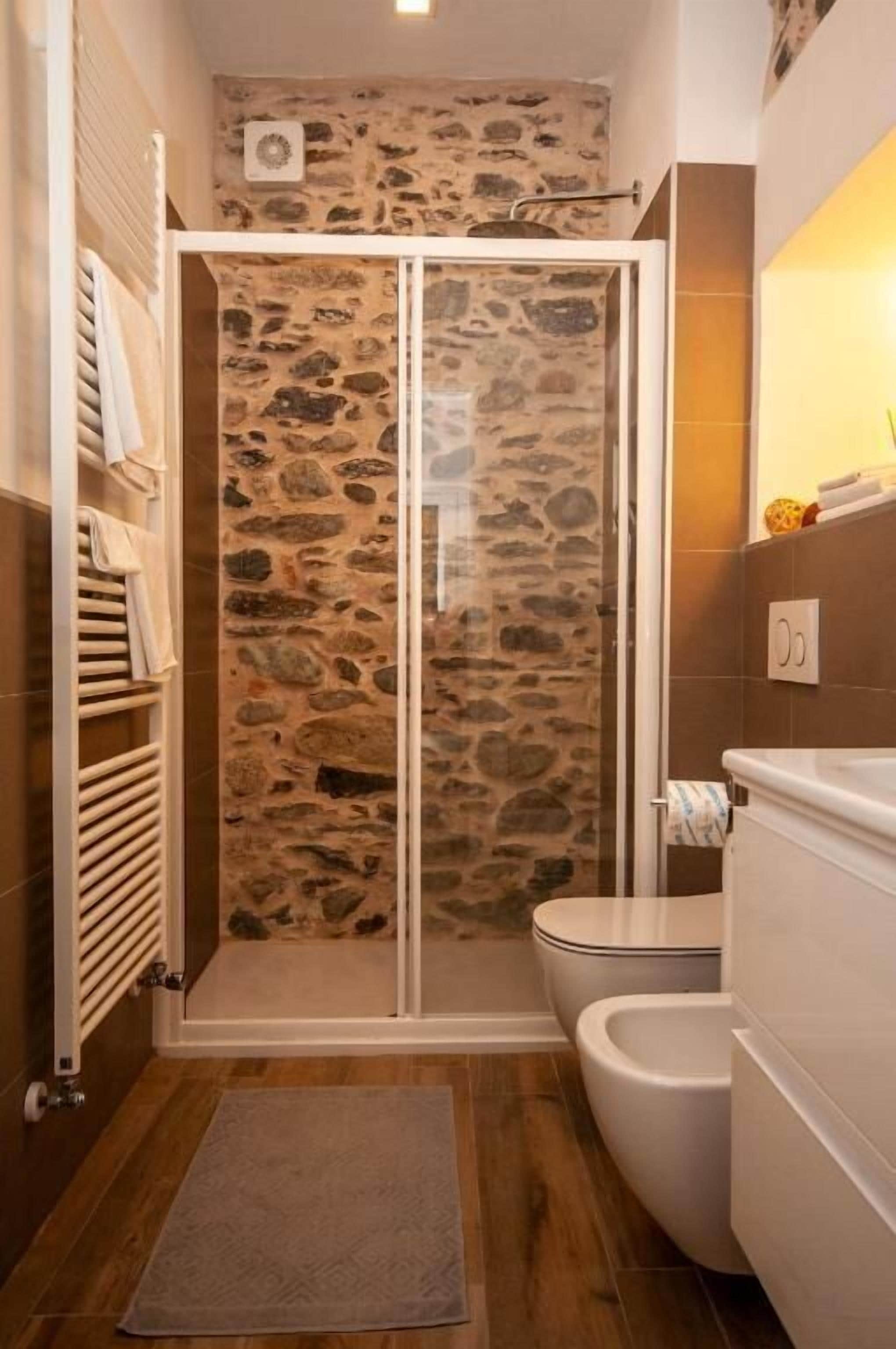 Une salle de bain avec une douche à l’italienne en pierre, des toilettes et un porte-serviettes.