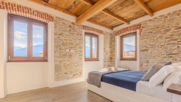 A bedroom with stone walls, wooden beams, and a bed with a blue blanket.