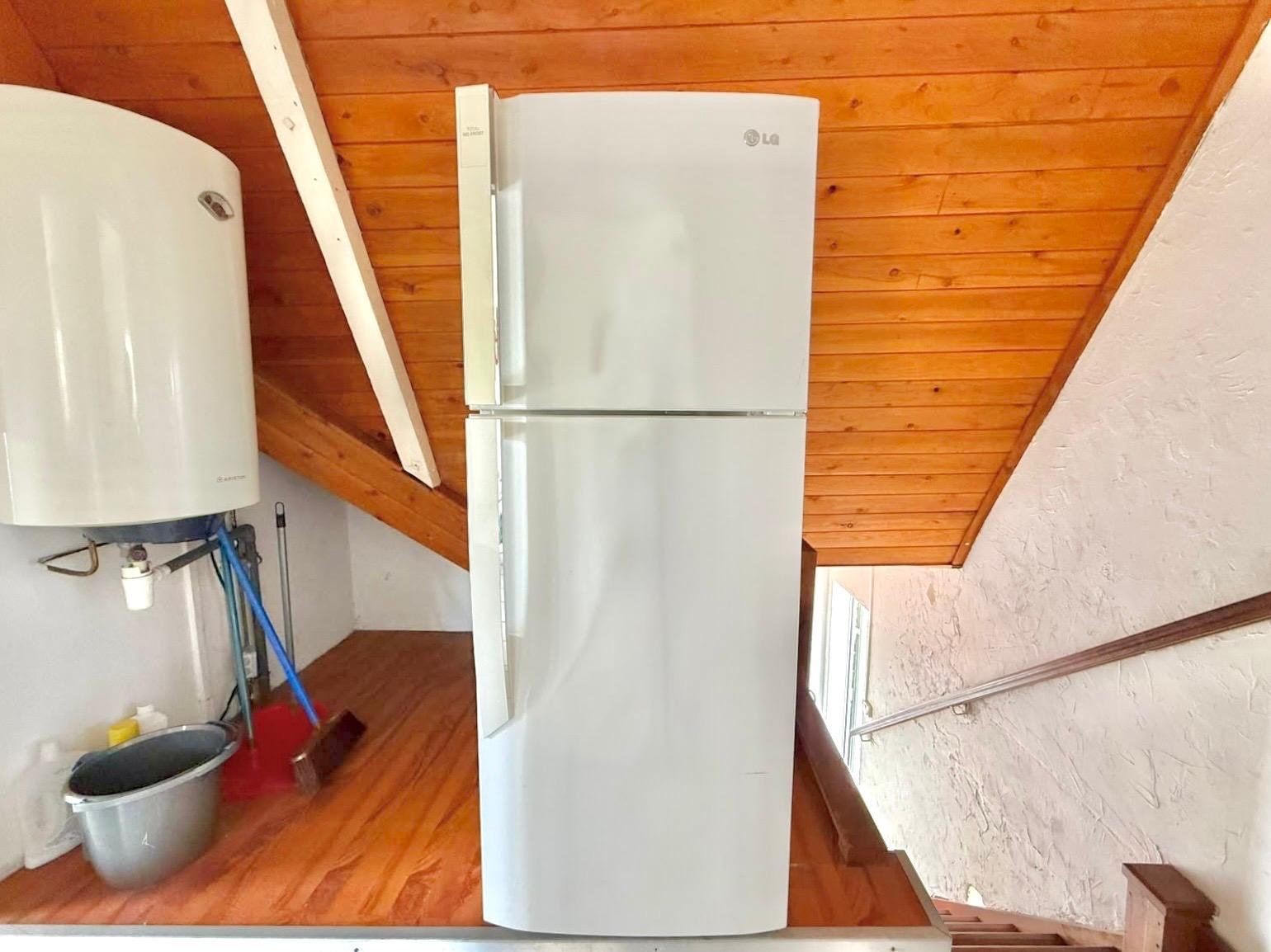 A compact kitchen with a white refrigerator, a water heater, and a metal pot on the floor.