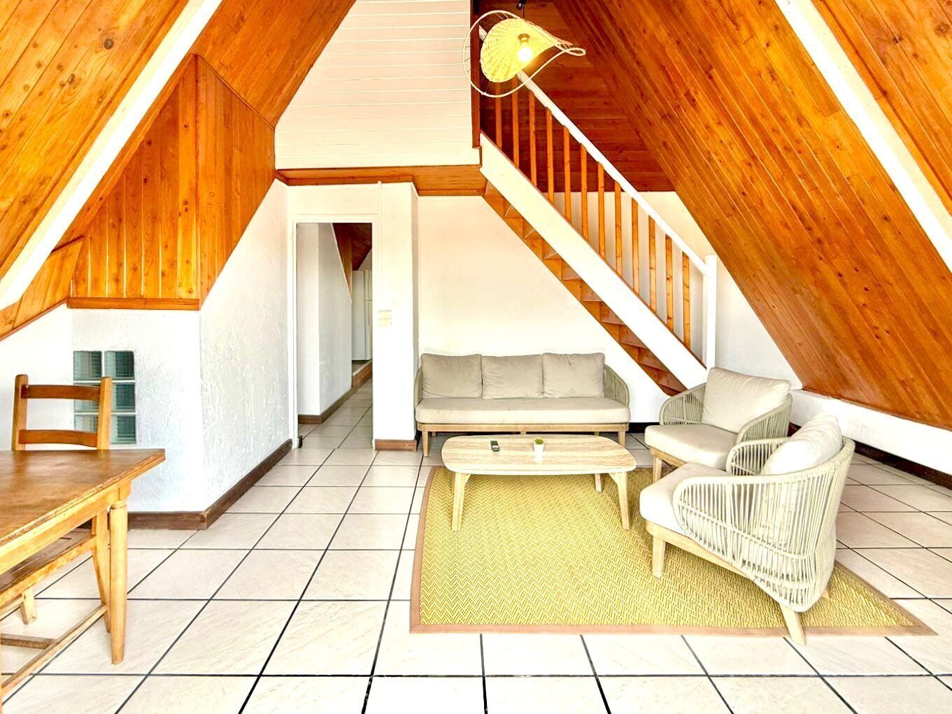 Een zolderkamer met een houten trap, een bank, een stoel en een eettafel.