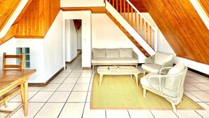 Ein Dachzimmer mit Holzboden und einer Wendeltreppe, einem Sofa, einem Sessel und einem Esstisch.