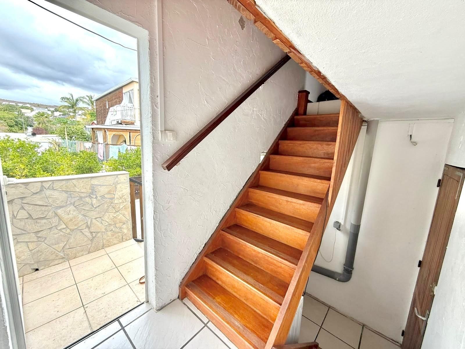 A wooden staircase leading to a balcony with a view of buildings and greenery.