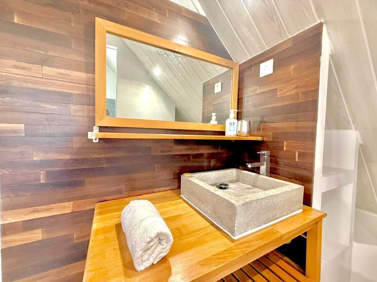 Une salle de bain avec un meuble-lavabo en bois, un lavabo rectangulaire, une serviette et un miroir.