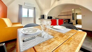 Comedor con mesa de madera preparada para cuatro personas, sofá amarillo y cocina al fondo.