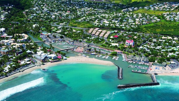 Vista aérea de un pueblo costero con un puerto deportivo, playa y zonas residenciales.